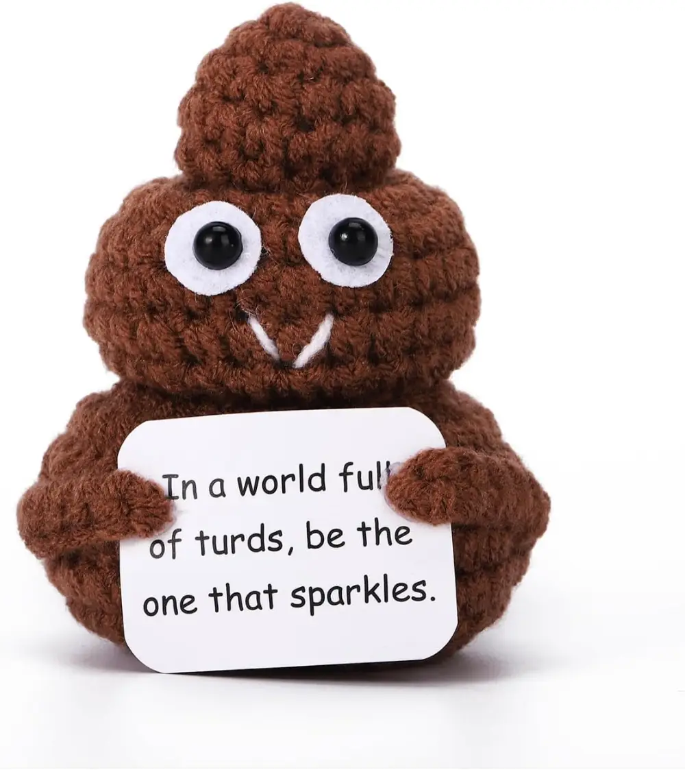 Knitted poop emoji plush holding a sign that reads, 'In a world full of turds, be the one that sparkles,' perfect for humorous gifts or desk decor.