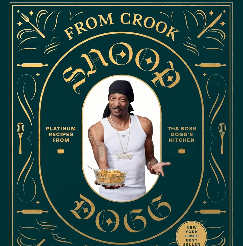 Hardcover copy of “From Crook to Cook: Platinum Recipes from Tha Boss Dogg’s Kitchen” by Snoop Dogg, a celebrity cookbook featuring soul food recipes, displayed standing on a white background.